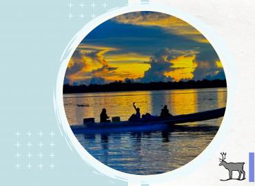 A Kayak with 3 people in it moving through the waves of a lake as the sun sets in the background