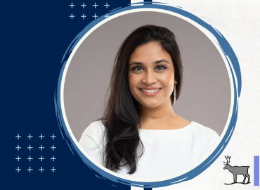 Professional headshot of the speaker of this seminar, Dr. Nadha Hassen. She is smiling towards the camera infront solid grey background.